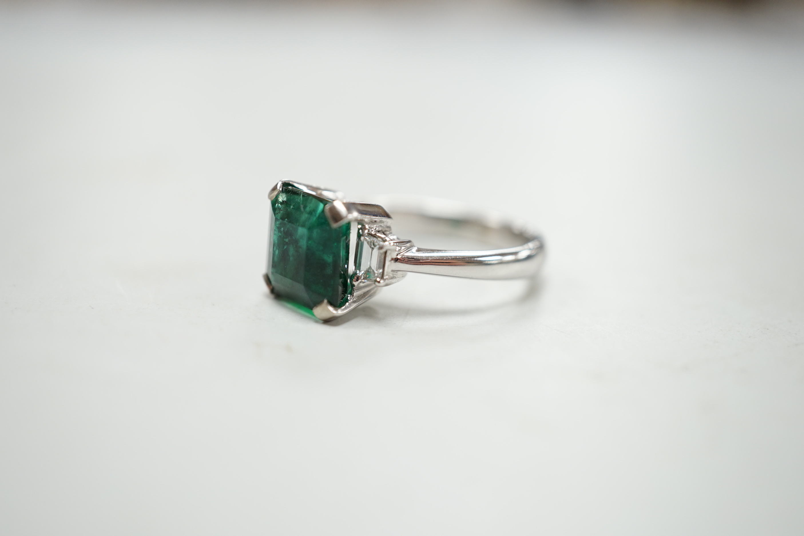 A modern 18k white metal and single stone emerald set ring, baguette cut diamond set shoulders, size N, gross weight 5.8 grams